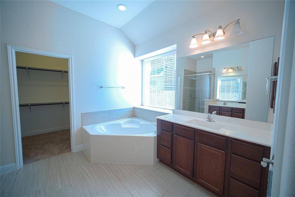 Luxurious master bathroom featuring a spacious soaking tub, elegant vanity with ample storage, and a sleek glass-enclosed shower. Natural light pours in, creating a serene and inviting atmosphere.