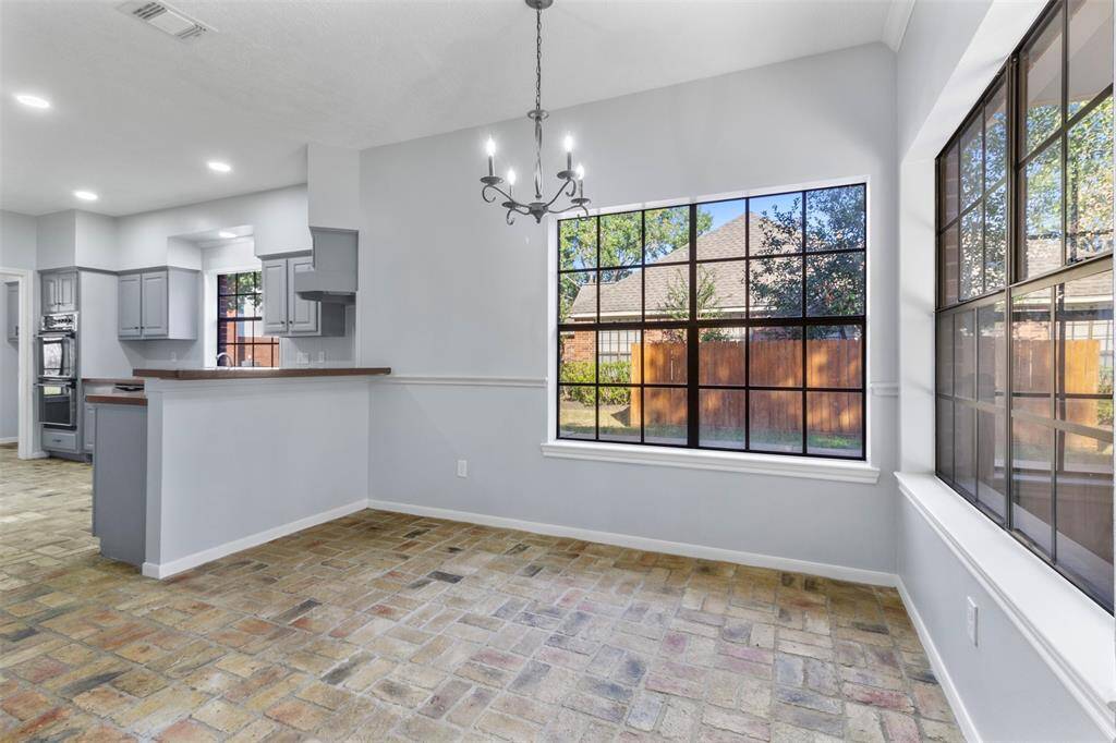 This bright and airy dining area features large windows with a view of the backyard, a stylish chandelier, and an open layout connecting to the modern kitchen with ample counter space and sleek cabinetry.