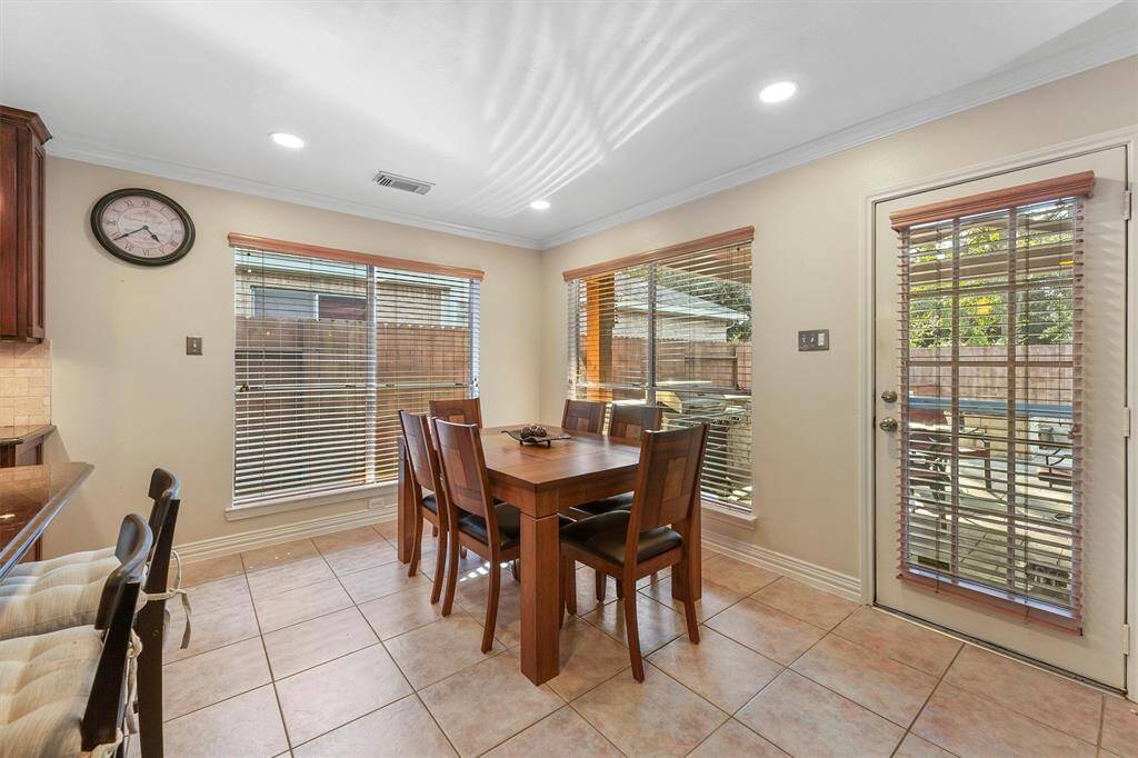 This is a bright and inviting breakfast room with tile flooring, ample natural light from large windows with blinds, and a glass door leading to an outdoor space.