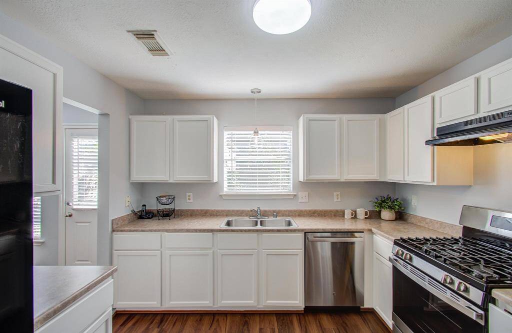 Bright kitchen with modern appliances, white cabinetry, and vinyl flooring. It features a large window above the sink, offering natural light, and ample counter space for cooking.