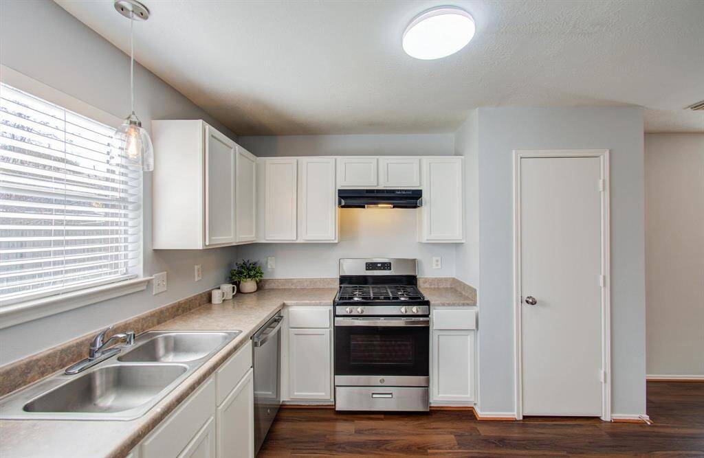 Bright kitchen with modern white cabinets, stainless steel appliances, and vinyl flooring. Features a double sink and ample counter space, with natural light from the window.