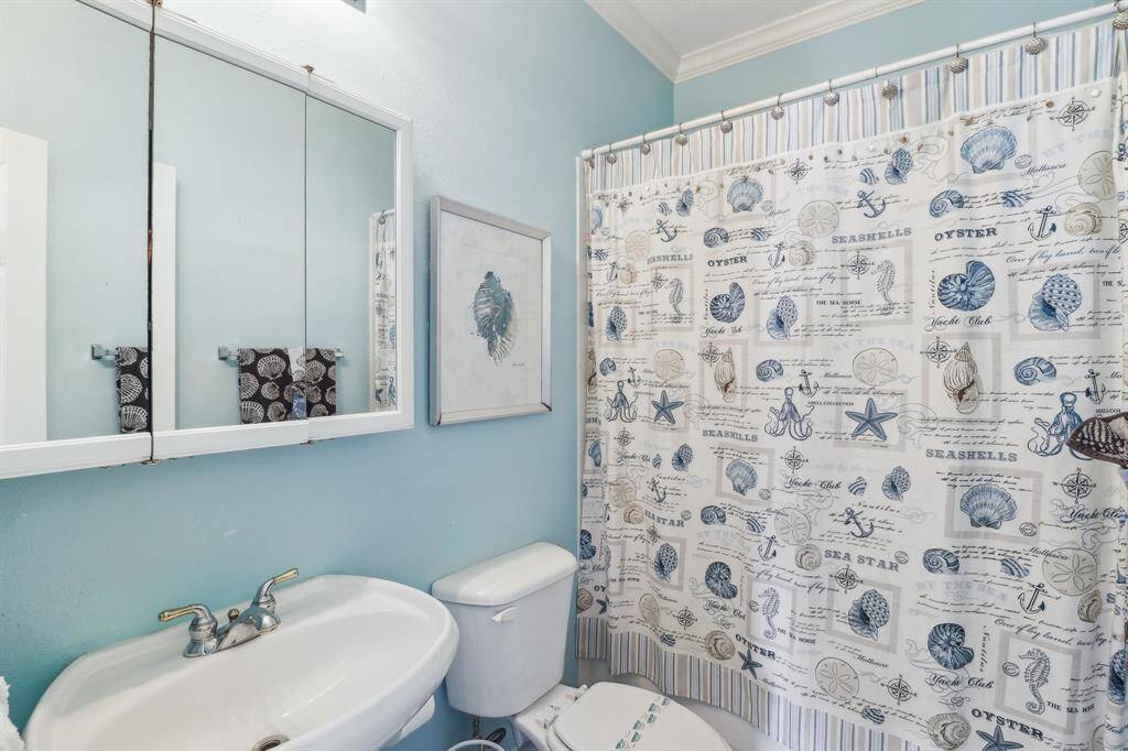 This charming secondary bathroom features a tub/shower combination, perfect for convenience and versatility. The coastal-inspired decor is highlighted by light blue walls and nautical accents, creating a refreshing and relaxing atmosphere. A mirrored medicine cabinet and pedestal sink provide functional storage and a clean, streamlined design.