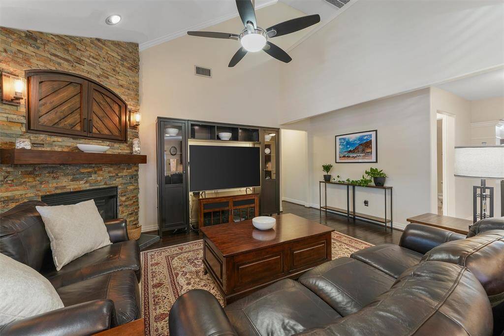 This is a cozy and inviting living room featuring a high ceiling with recessed lighting, a ceiling fan, a stone fireplace, and warm wood accents.  The space is well-lit and open area offering a seamless flow for entertaining and daily living.