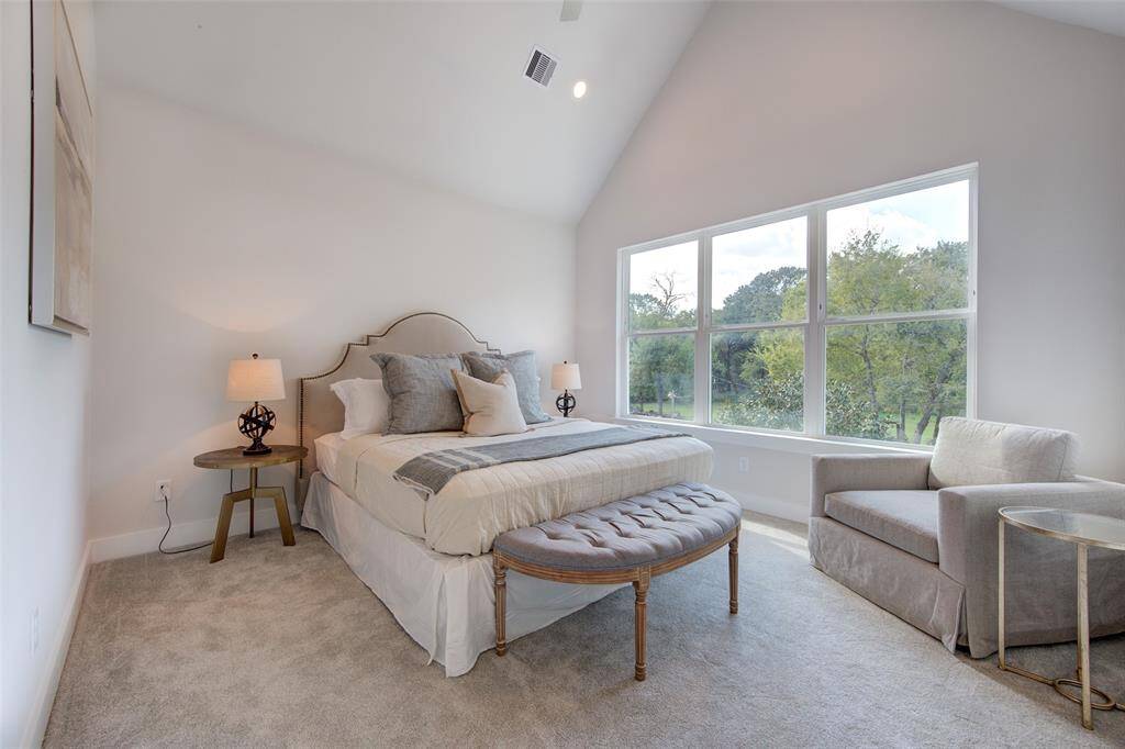 This primary bedroom is a tranquil retreat with large windows offering beautiful views and plenty of natural light. The vaulted ceiling adds a sense of spaciousness, while the cozy seating area is perfect for relaxing.