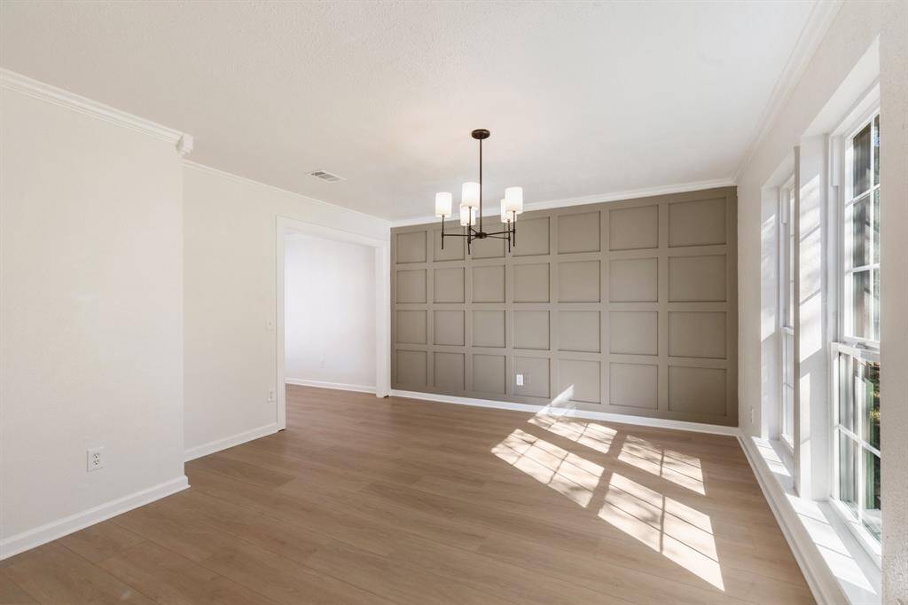 This dining room features large windows for natural light, a modern chandelier, and a stylish accent wall.