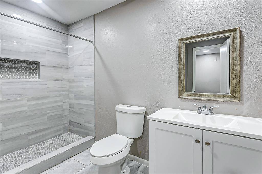 The modern bathroom features a beautifully tiled shower with hexagon tile accents for a luxurious touch. A sleek vanity with a framed mirror adds rustic charm to the contemporary design, making this space both functional and elegant.