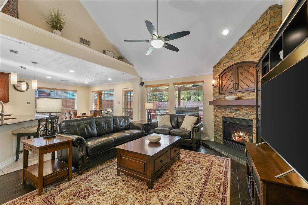 This is a cozy, well-lit living space with an open layout that connects to the kitchen. The room is complemented by hardwood floors and large windows providing ample natural light.
