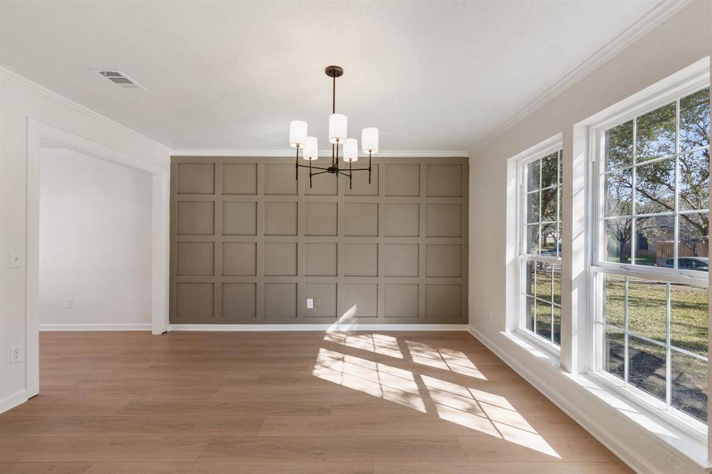 This dining room features large windows for natural light, a modern chandelier, and a stylish accent wall.