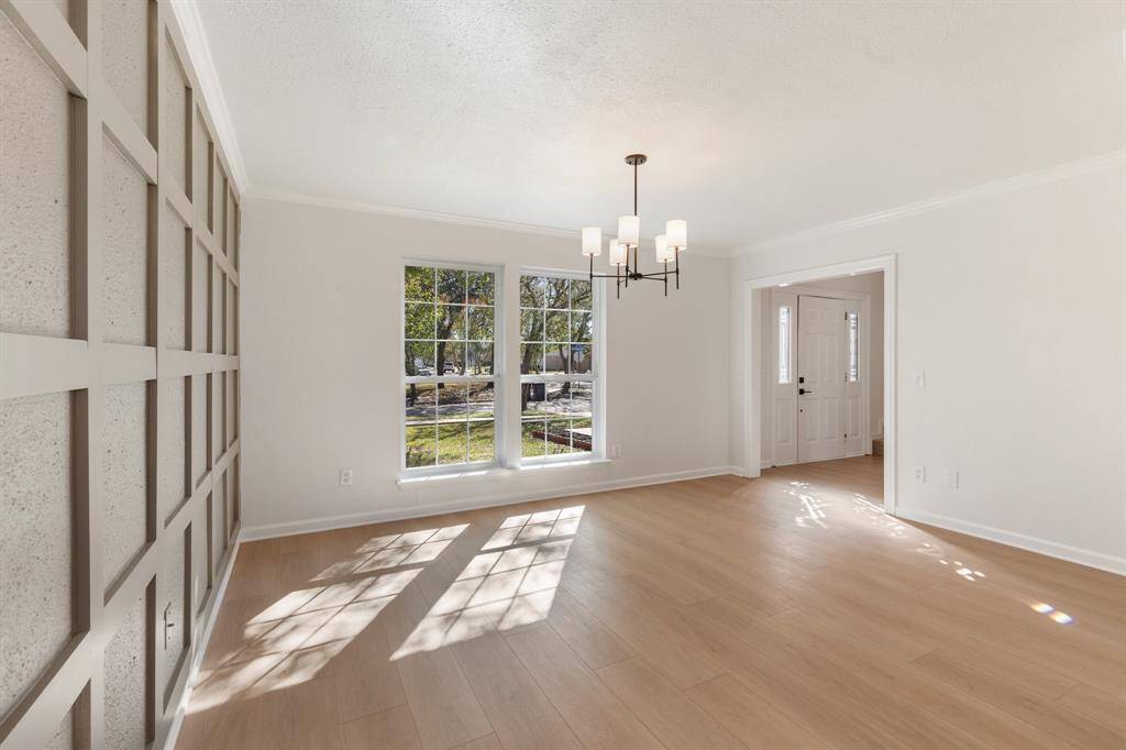 This dining room features large windows for natural light, a modern chandelier, and a stylish accent wall.