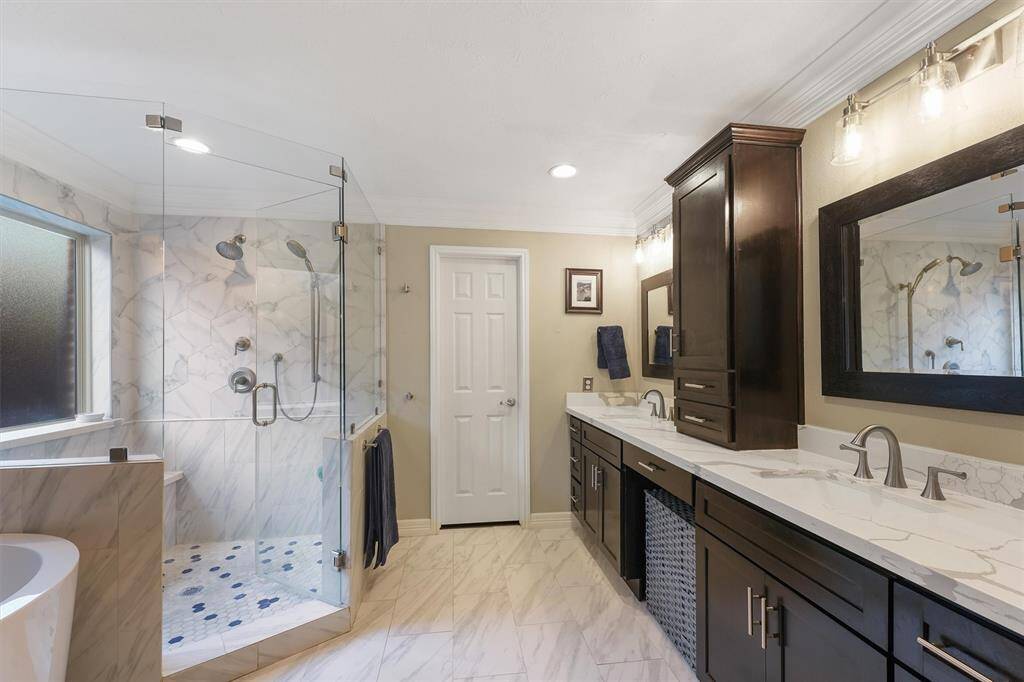 This spacious updated  primary bathroom features a large walk-in shower with a seamless glass enclosure, dual vanity sinks with a generous counter space, and dark wood cabinetry.