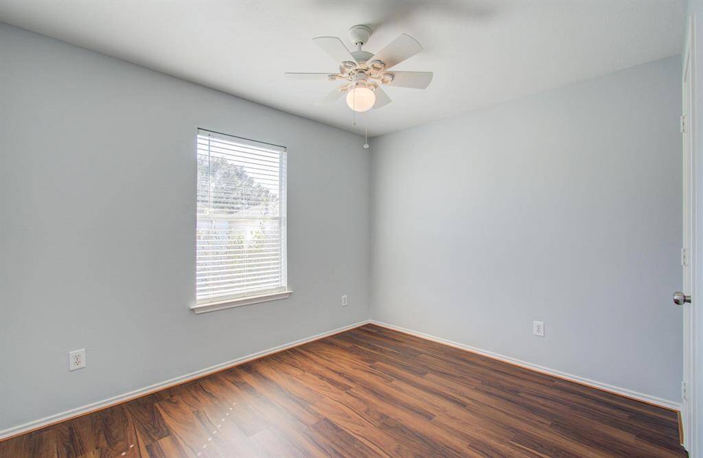 Second bedroom has light gray walls, vinyl flooring, and a ceiling fan. It features a window that lets in natural light, creating a cozy and inviting atmosphere.