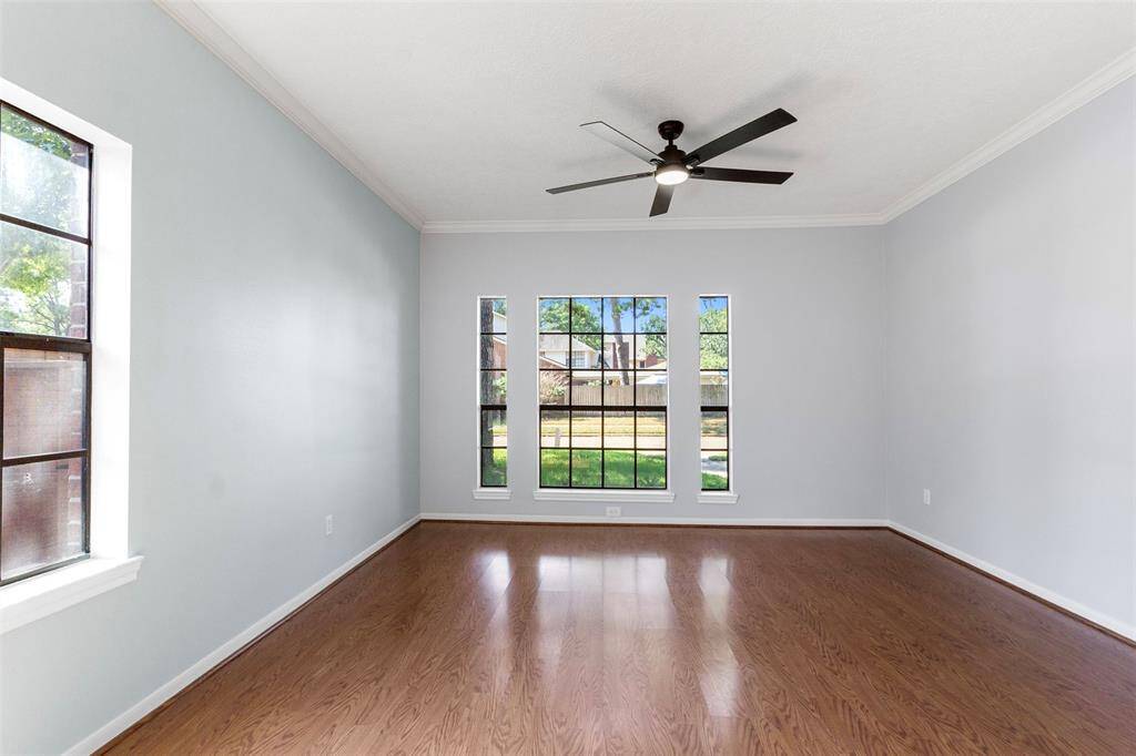 This spacious Master bedroom features large windows for natural light, elegant wood flooring, and a modern ceiling fan, creating a bright and inviting atmosphere.