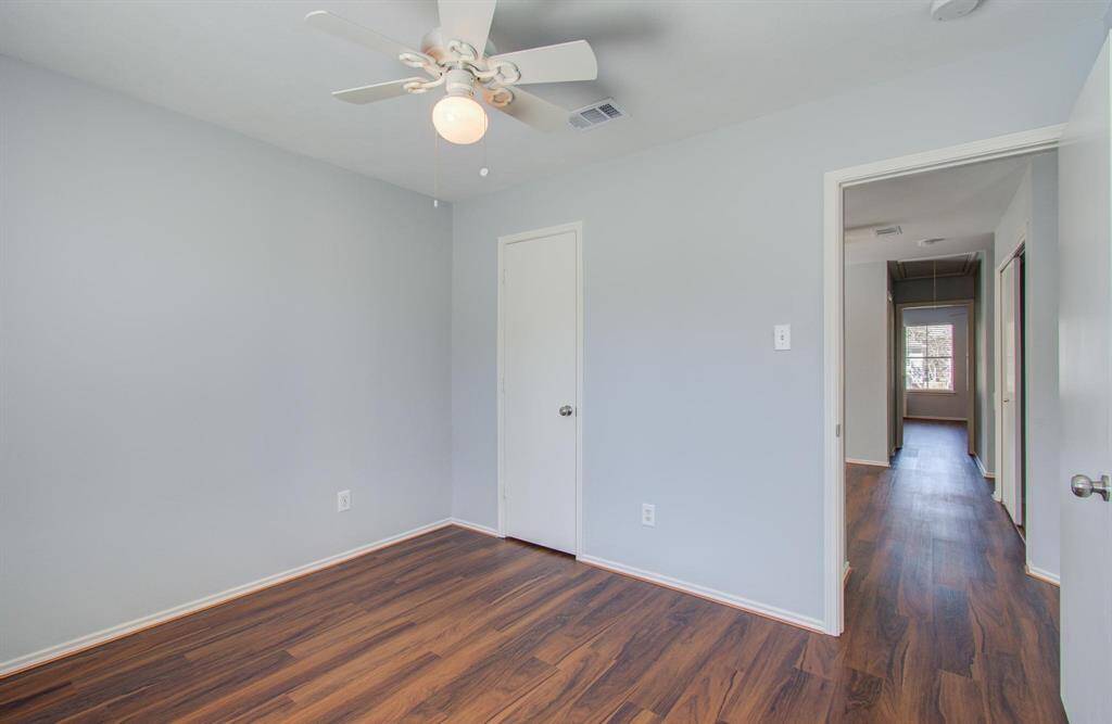 Another view of second bedroom offering a clean and neutral space. The doorway leads to a hallway with natural light from a window at the end.