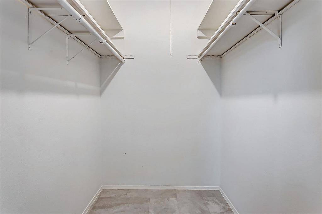 Maximize your storage with this walk-in closet, featuring dual rods and shelves to organize clothing, accessories, and more. The clean white walls and neutral flooring provide a fresh and spacious feel, perfect for staying organized in style.