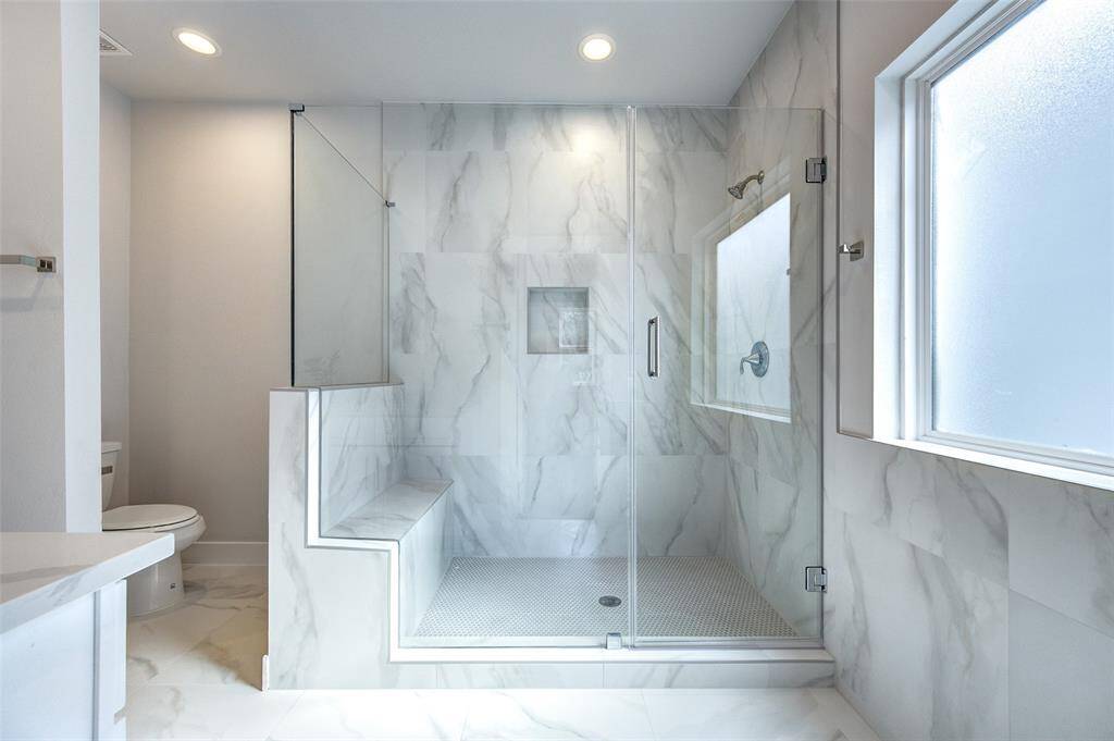 This luxurious bathroom boasts a spacious walk-in shower with frameless glass doors and marble tile surrounds. The built-in bench and recessed lighting create a serene and spa-like atmosphere.