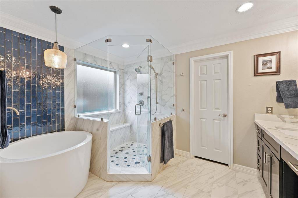 Another view of a the primary bath  featuring the freestanding bathtub, a separate glass-enclosed shower  and elegant tile flooring. The room is well-lit with a combination of natural and stylish pendant lighting.