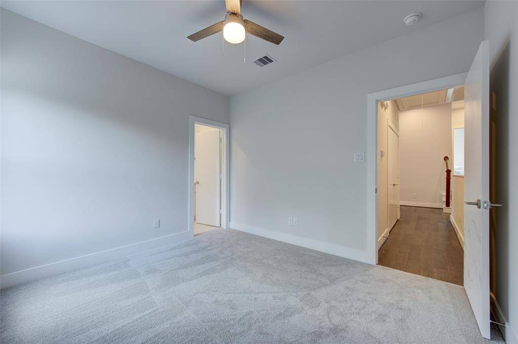 A spacious second bedroom with plush carpeting and a ceiling fan, perfect for guests or family members. The room's neutral tones and ample natural light create a calming and comfortable environment.