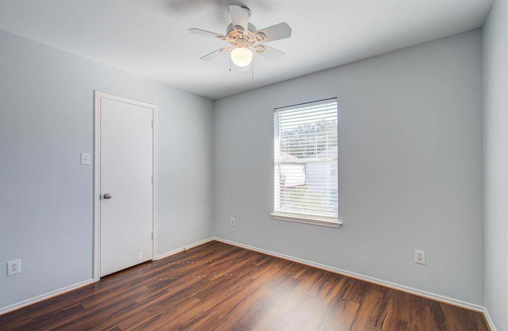 Third bedroom features fresh light gray walls, a ceiling fan, vinyl flooring, and a window, creating a cozy and inviting space.