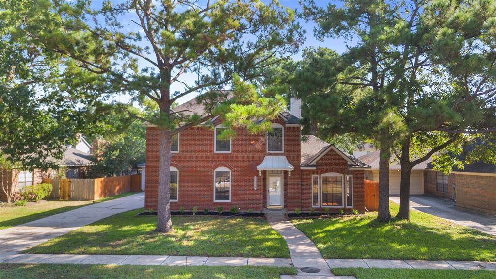 Charming two-story brick home with a welcoming front path, shaded by mature trees. Features a double driveway and a cozy front porch, set in a quiet, leafy neighborhood.