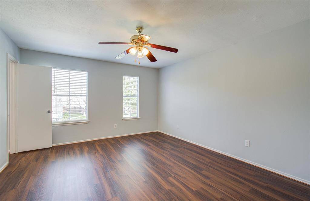 Primary bedroom is a bright, spacious room featuring luxury vinyl flooring, neutral walls, two windows for natural light, and a ceiling fan for additional ventilation.