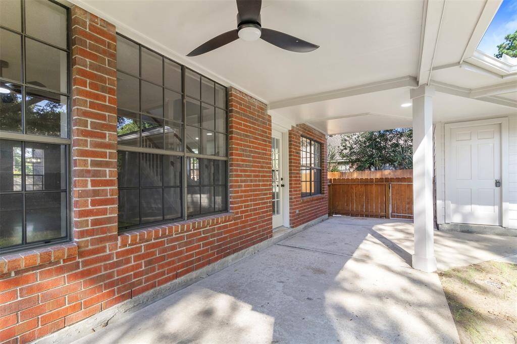 This photo showcases a covered patio area with a ceiling fan, red brick exterior, large windows, and a wooden fence, providing a cozy outdoor space for relaxation or entertainment.