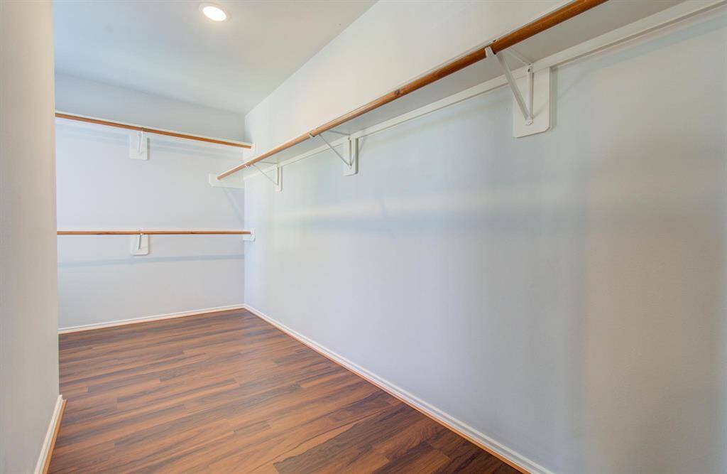 Spacious walk-in closet with luxury vinyl flooring, ample hanging space, and soft overhead lighting.