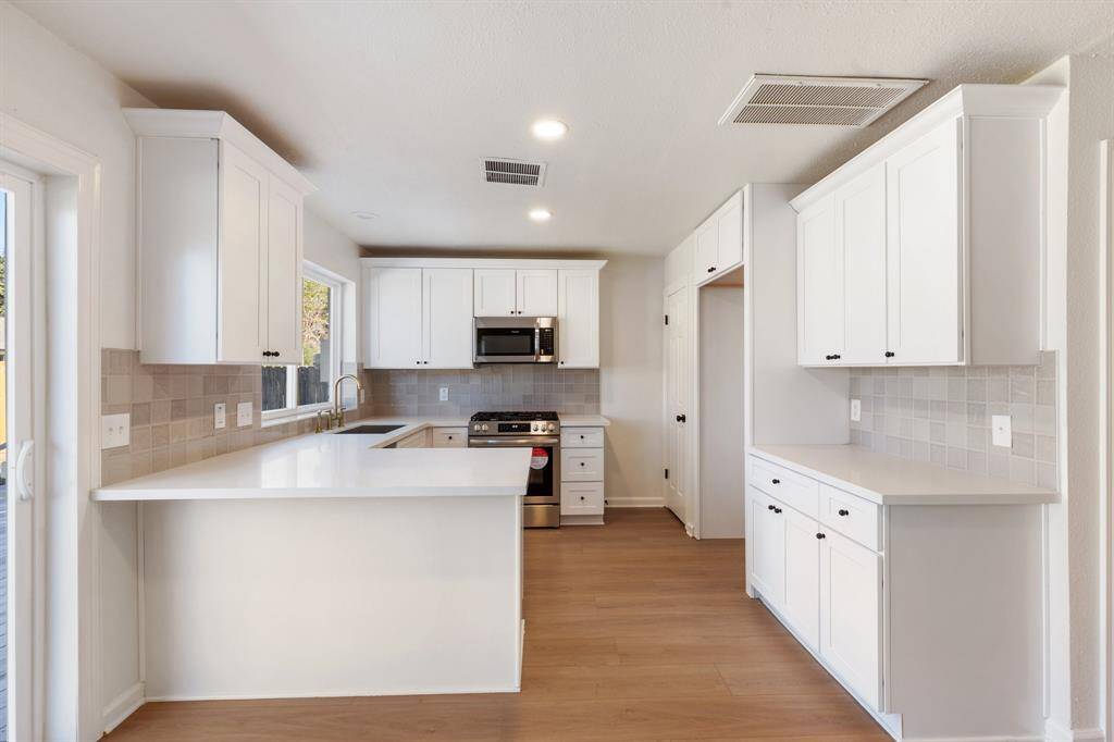 Bright, modern kitchen with white cabinetry and stainless-steel appliances. Features ample natural light and an open layout, perfect for cooking and entertaining.