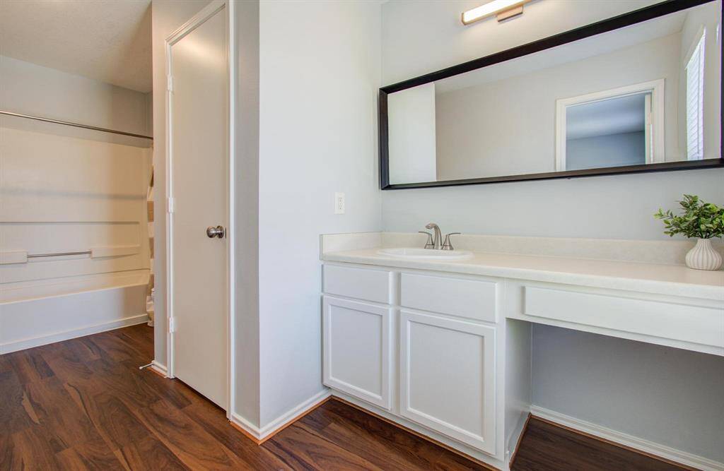 Primary bathroom features a clean, modern design with light walls, a large mirror, and sleek white cabinetry. It includes a bathtub with a shower and a spacious vanity area.
