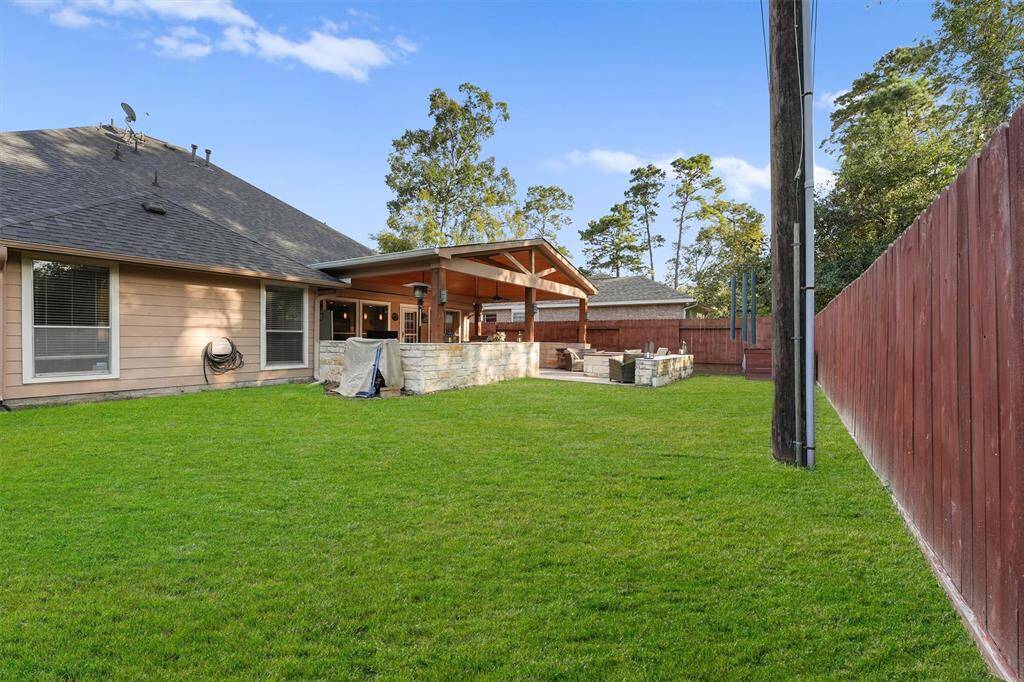 This spacious backyard has a well-maintained lawn and a privacy fence. The house features a covered patio area, perfect for outdoor entertaining. Mature trees can be seen beyond the fence.