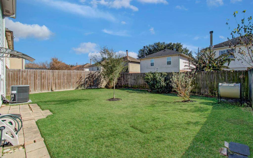 Spacious backyard with a well-maintained lawn, a few small trees, and shrubs. It's enclosed by a wooden fence, providing privacy. The area is suitable for outdoor activities and relaxation.
