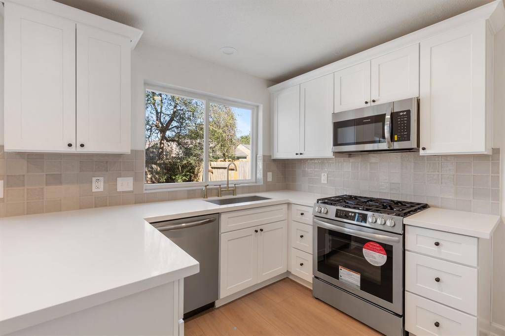 This kitchen features modern white cabinetry, stainless steel appliances, and a large window for natural light, creating a bright and inviting space.