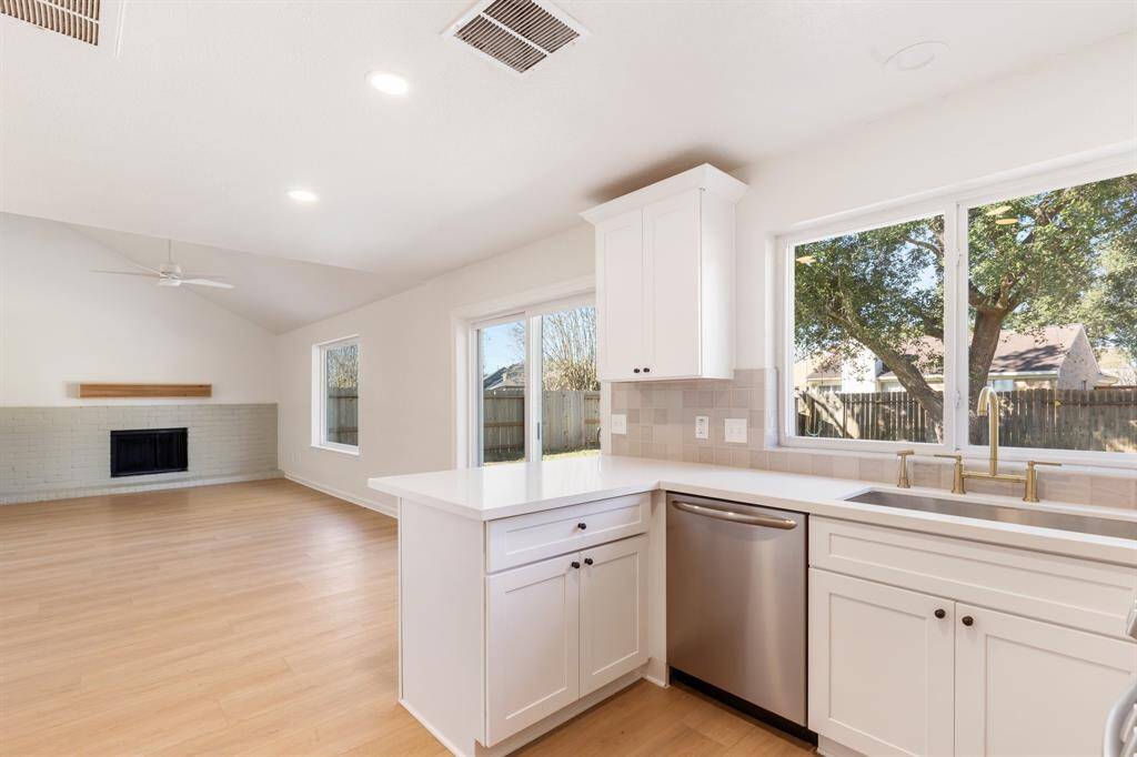 This kitchen features modern white cabinetry, stainless steel appliances, and a large window for natural light, creating a bright and inviting space.