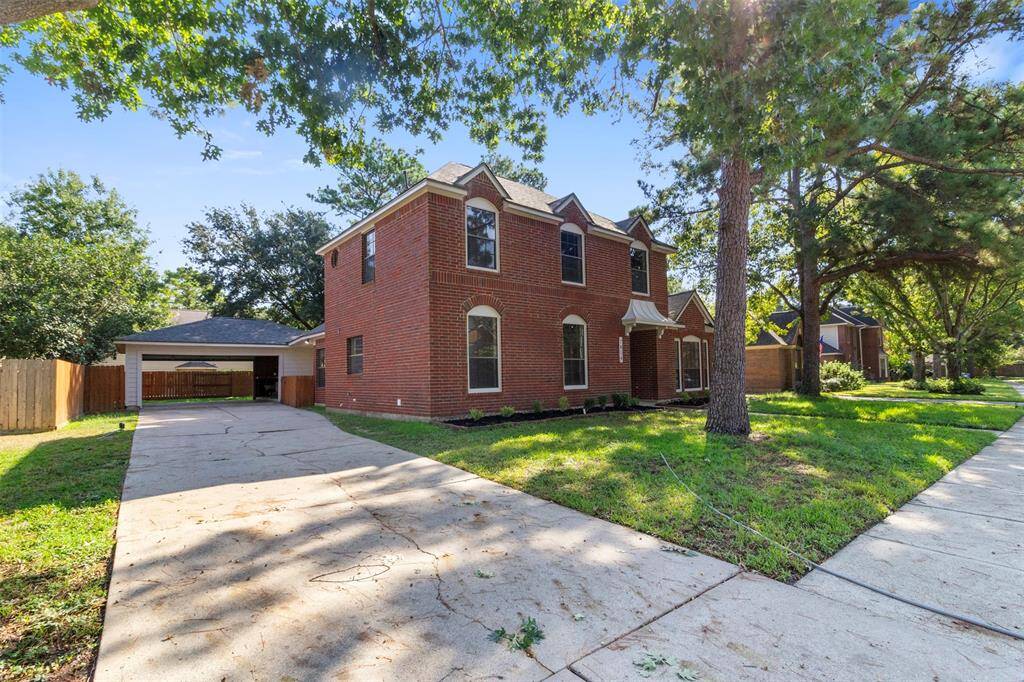This photo shows a charming two-story brick home with a spacious driveway, surrounded by mature trees and a well-maintained lawn. The property includes a detached garage and is situated in a peaceful neighborhood.