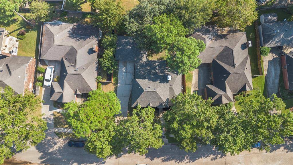 This aerial photo shows a suburban neighborhood with several single-family homes, each with a driveway and surrounded by trees. The houses have similar roofing styles, and the area appears peaceful with ample greenery.
