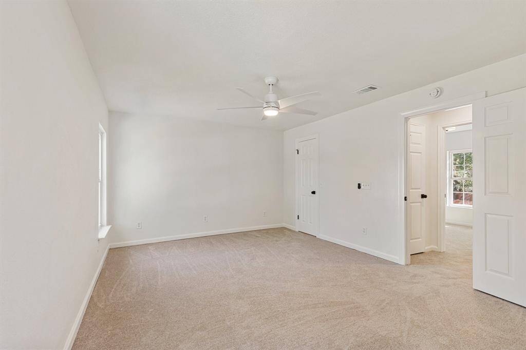 Bright and spacious primary bedroom featuring large windows for natural light and a ceiling fan, ideal for relaxation.