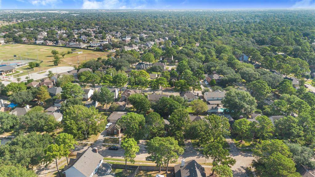 This aerial photo showcases a lush, green neighborhood with tree-lined streets and well-spaced homes. The area includes nearby recreational facilities and has a serene, suburban feel, ideal for family living.