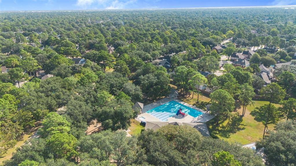This aerial photo shows a vibrant, tree-filled neighborhood with a community pool and playground, suggesting a family-friendly environment with ample green space.