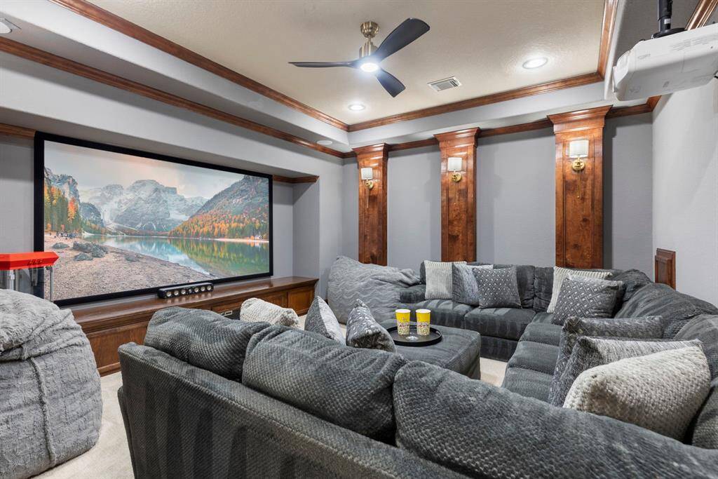 The media room is truly one-of-a-kind, featuring a projector, projector screen, receiver, stunning woodwork, a modern ceiling fan, and built-in cabinet storage. For added convenience, there's also a built-out attic space behind the sofa.