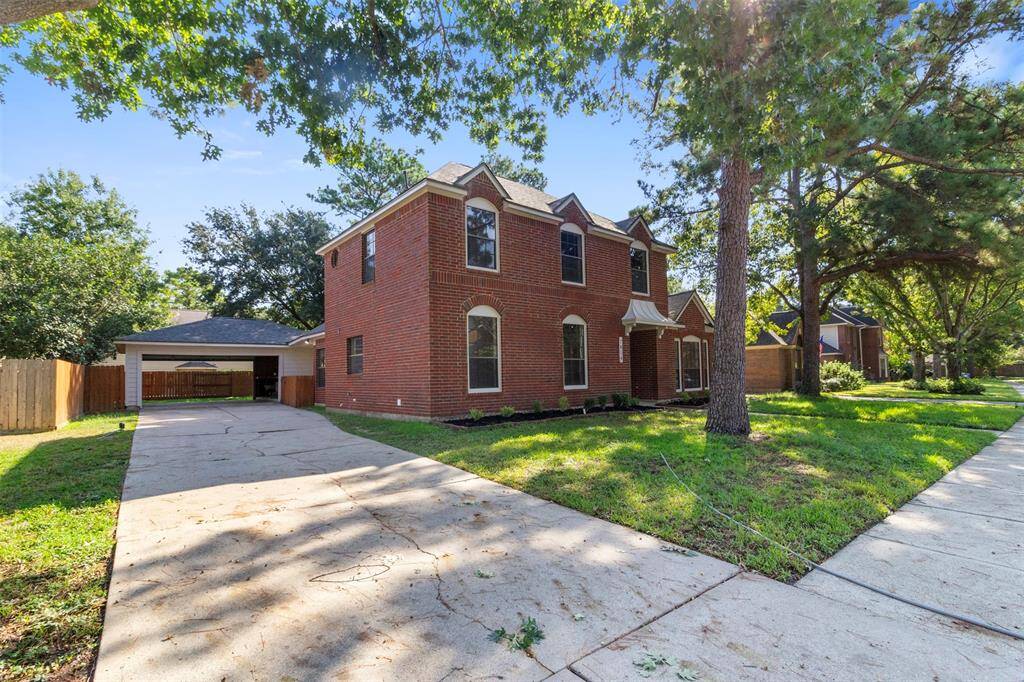 This charming two-story brick home features a spacious driveway, a detached garage, and is surrounded by lush greenery and mature trees, offering both curb appeal and privacy in a serene neighborhood setting.