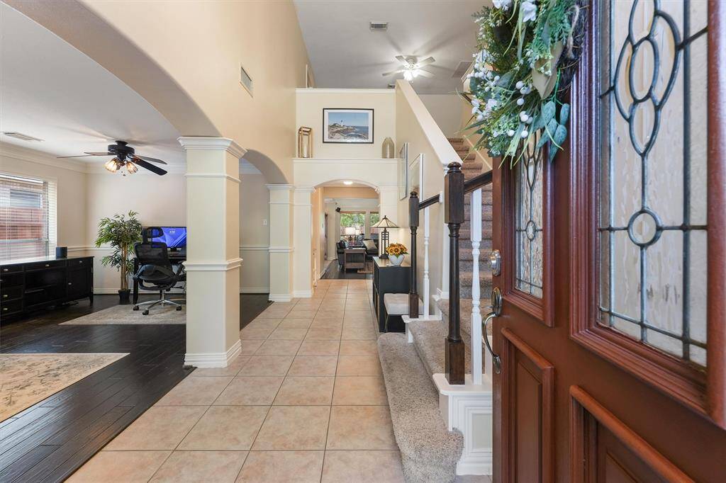 This spacious, well-lit interior features tiled flooring, elegant columns, high ceilings with ceiling fans, and a neutral color palette.