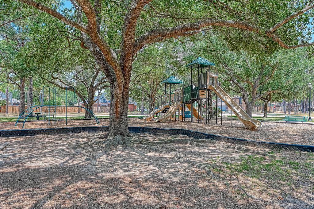 This photo showcases a well-shaded playground with slides and climbing structures, surrounded by mature trees. It's an inviting space for families in a serene neighborhood setting.