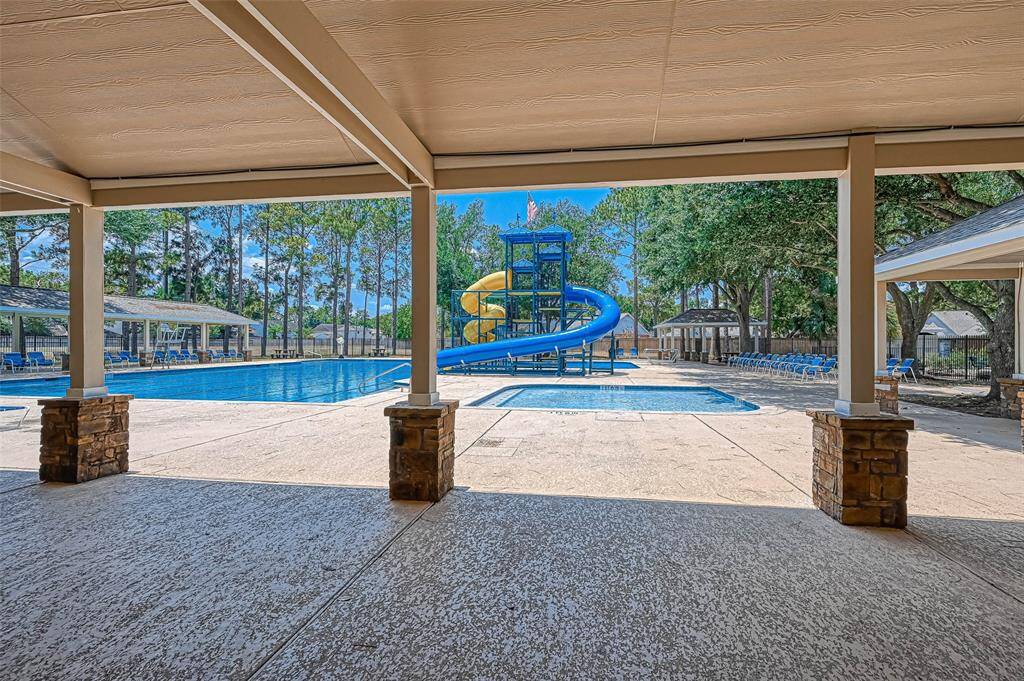 This photo shows a community swimming pool area with a large water slide, surrounded by a spacious deck and shaded seating. The setting is enhanced by mature trees, providing a relaxing and fun environment for residents.