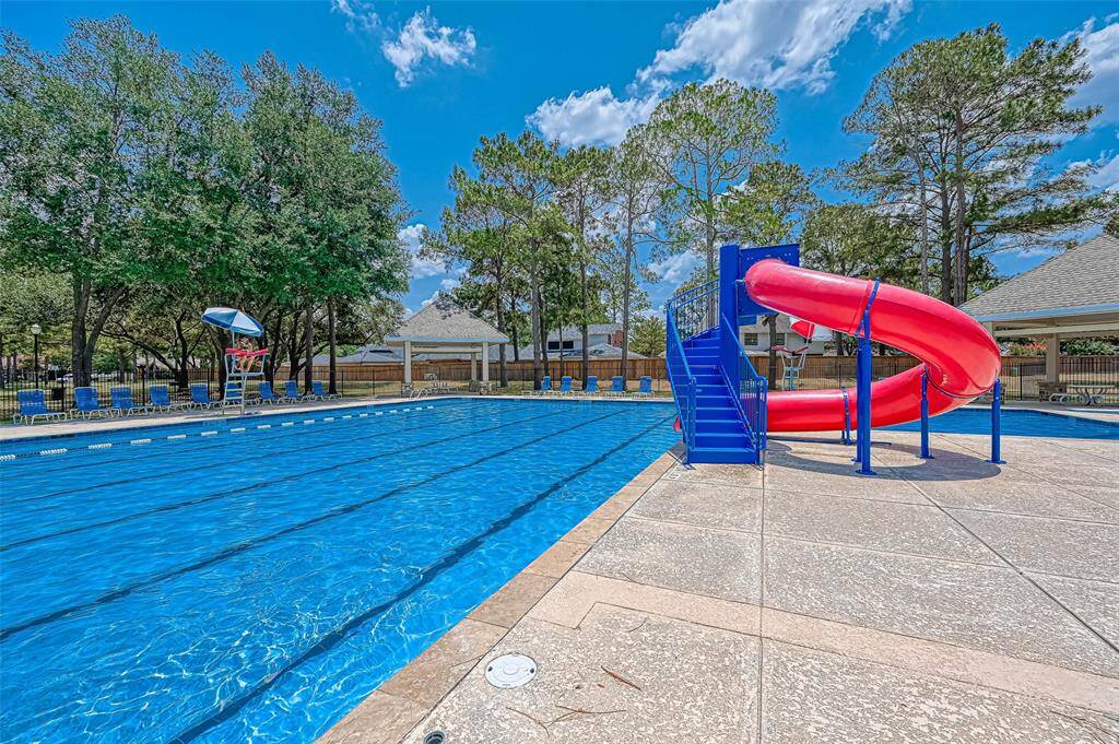 This photo showcases a community pool area featuring a large swimming pool with lanes, surrounded by trees and lounge chairs. It includes a vibrant red water slide, providing a fun and inviting space for relaxation and recreation.