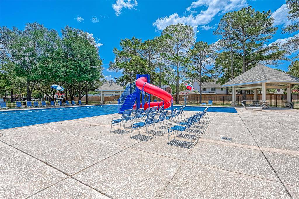 This photo showcases a community pool area with a large slide, surrounded by trees. There's ample seating and a covered pavilion, perfect for relaxation and gatherings.