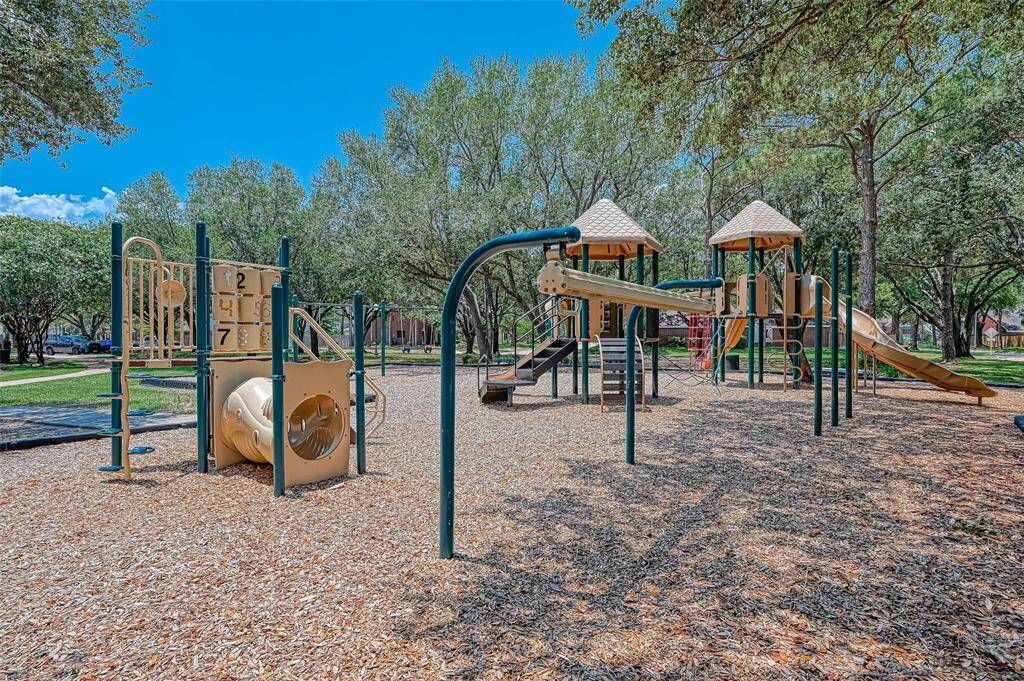 This photo shows a spacious playground with multiple play structures, slides, and climbing areas, surrounded by trees and green space, ideal for families with children.