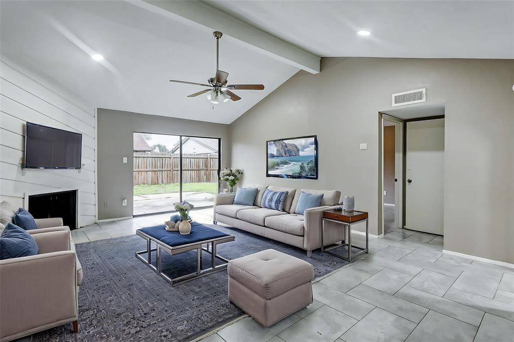 Step into the bright and airy living room, a perfect blend of comfort and style. High ceilings and sleek tiled floors create a spacious atmosphere, while the shiplap accent wall with a cozy fireplace adds a touch of rustic charm. The sliding glass doors provide seamless access to the backyard, inviting in natural light and offering a lovely view of your private outdoor retreat.