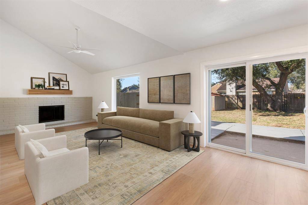 Spacious open living space features a vaulted ceiling, a cozy fireplace, and abundant natural light creating a warm, inviting atmosphere. (virtually staged)