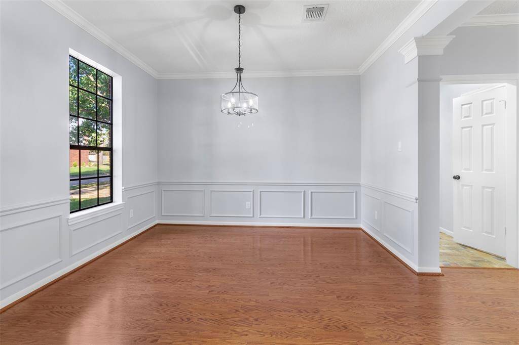 This room features elegant wainscoting, hardwood floors, and a large window for natural light. It has a modern chandelier and neutral wall colors, offering a versatile space for dining or gathering.