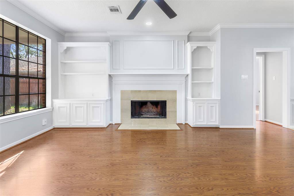Bright, spacious living room with hardwood floors, a central fireplace, built-in shelves, and large windows offering plenty of natural light.