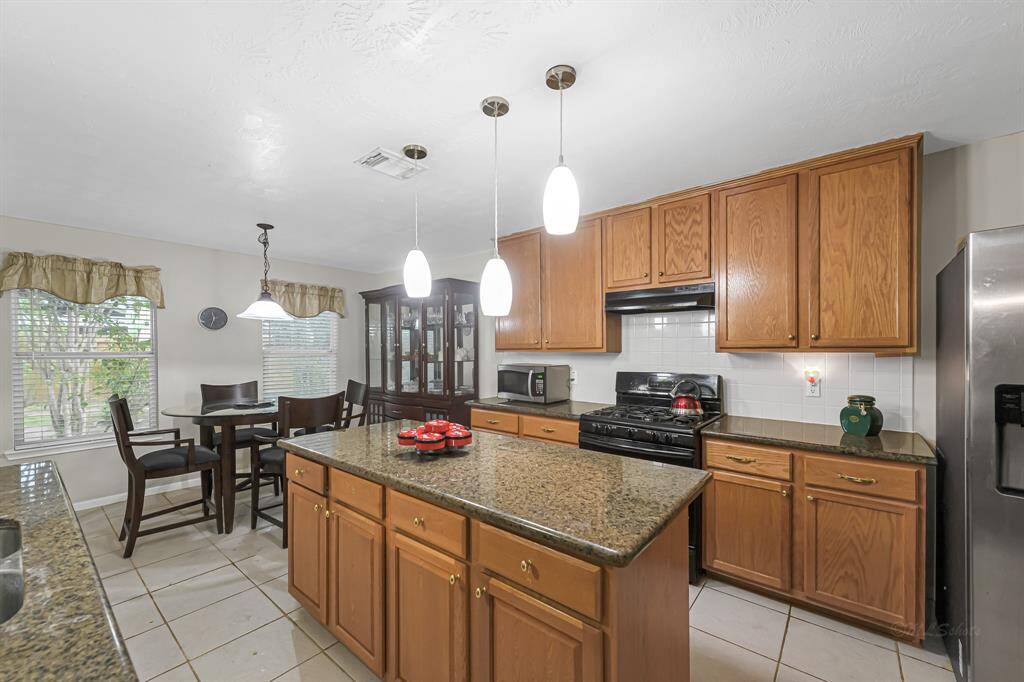 Continuing on, you'll find your bright and spacious kitchen with a warm and inviting atmosphere. The kitchen features wooden cabinets and granite countertops, with a large island in the center that offers additional prep space and seating. Three updated pendant lights hang above the island, providing ample lighting.